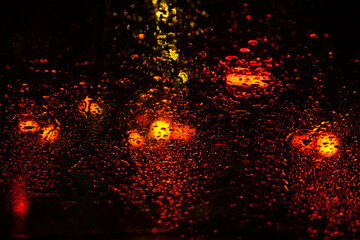 Fototapeta na wymiar Rain drops on glass surface with red bokeh night city lights from a lanterns, car, shops