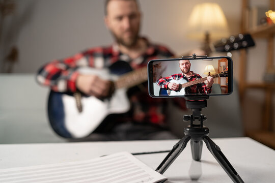 Guitar tutorial with smartphone. Teacher teaching how to play an instrument. Online music course. Man use mobile screen recording online music at home.