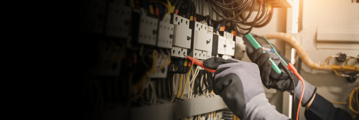 Electricity and electrical maintenance service, Engineer hand holding AC multimeter checking electric current voltage at circuit breaker terminal and cable wiring main power distribution board.