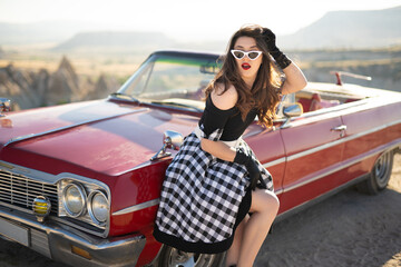 beautiful girl in retro style posing near vintage red cabriolet car.