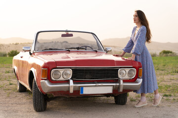 beautiful girl in retro style posing near vintage red cabriolet car.