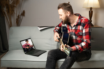 Man playing guitar and give online lesson on laptop for student practicing at home. Stay home. Virtual musical teacher. Online training