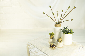 Branches in buds and young leaves in a vase in the interior. Composition of quail egg and green moss on a stand. The idea of festive decoration of the room for Easter. High quality photo