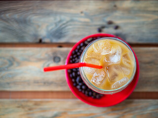 Ice coffee on a wood table with ice and red straw, coffe beans and red saucer on background. Cold summer drink with red tube