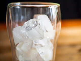 a glass filled with ice on top of a wooden table, black background on background
