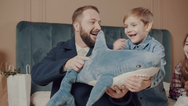 Dad gives his son a plush shark toy as a gift. The joy of a son. Dad hugs his son. Happy family.