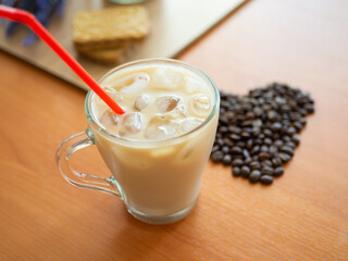 a cup of coffee with ice and a red straw next to a heart shaped pile of coffee beans, cookies on background.