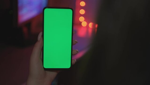 Mobile phone in hand. Holding smartphone with red blue neon lighting on dark background. Green chromakey screen with markers. 4K