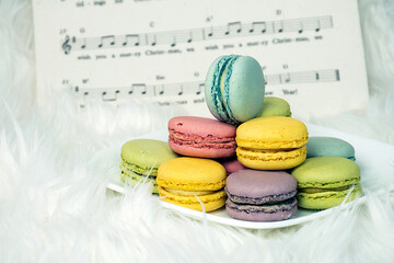Colorful macarons on white square plate and fluffy fur with Christmas sheet music background