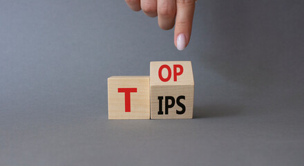 Top Tips symbol. Businessman hand points at turned wooden cubes with words Top Tips. Beautiful grey background. Business and Top Tips concept. Copy space