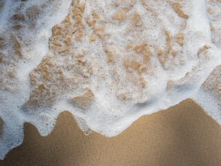 Sand beach with surfing wave of water for banner background. Bubble wave on the beach