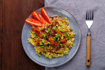 Chicken rice in teriyaki sauce garnished with green onions on a wooden table next to soy sauce on the table on a napkin next to a fork.