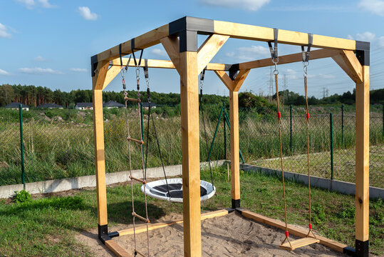A modern cube playground made of wood and metal corners, standing in the yard behind the house.