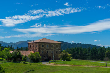 An old brick manor a tiled roof against the backdrop of mountains and green grass. Basque Country,...