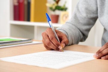Close up of black man hands signing document on a desk at home