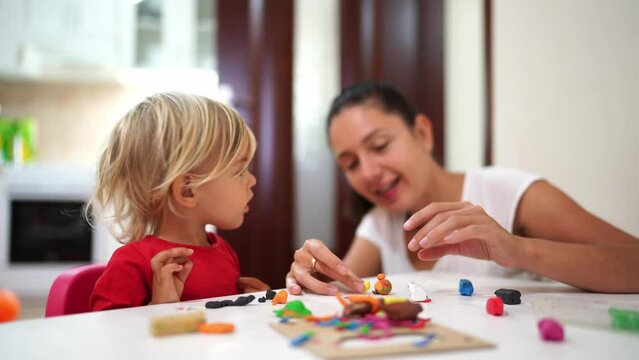 Mom teaches a little girl to roll out plasticine and sculpt figures at the table