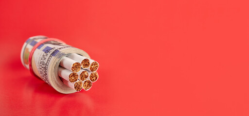 A roll of 100 dollar bills with cigarettes on a red background. Concept of expensive cigarettes.