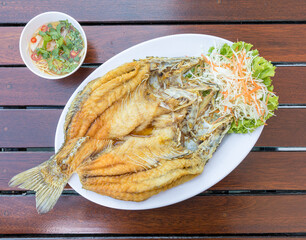 fried snapper fish Blank in white plate on wood table served with fish sauce and vegetables.
