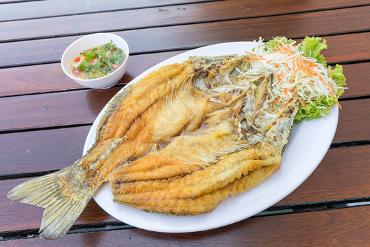 fried snapper fish Blank in white plate on wood table served with fish sauce and vegetables.