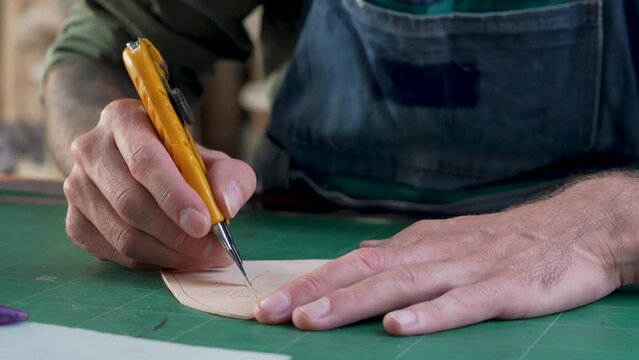 4K, Close-up handcrafted leather worker sits farts cowhide with cutter according pattern drawn on leather, meticulous for beautiful sharp focus, in order make cow leather good piece work.