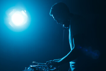 Silhouette of DJ mixing vinyl records on party in night club. Disc jockey playing techno music set...