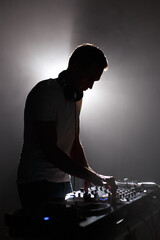 Silhouette of club dj mixing techno music. Young white man perfroming as a disc jockey on party in...