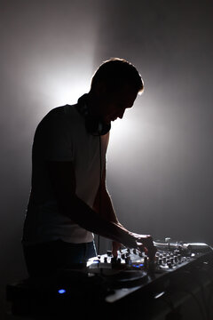 Silhouette of club dj mixing techno music. Young white man perfroming as a disc jockey on party in dark night club