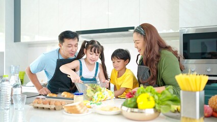 Obraz na płótnie Canvas Happy Asian family in the kitchen cooking together healthy. Parents teach little children healthy habits and how to mix vegetables in salad bowl