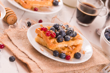 Waffles with red currant and blueberries on white dish.