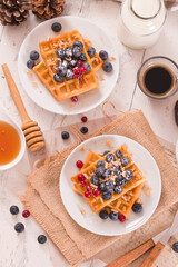 Waffles with red currant and blueberries on white dish.