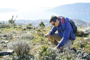 A young man collects mountain herbs against the backdrop of the sea. A tourist plucks useful plants...