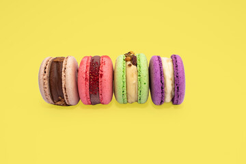 Sweet colorful macarons isolated on yellow background. Tasty red, green, brown, violet macaroons.