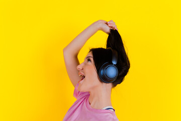 Portrait of a charming, joyful music lover holding, pulling pigtails or hair in her hands against a bright yellow background. Emotions, lifestyle, leisure, music, and dance concept.