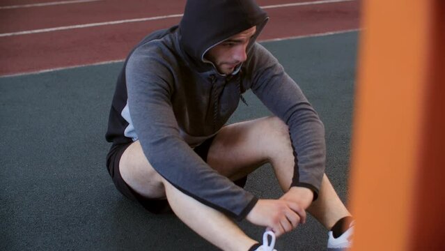 Athlete young man is sitting on floor and resting relax in gym wearing sportswear. He is deeply breathing. Tired exhausted sportsman. Workout training sport and active lifestyle concept. Male leisure.