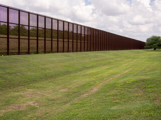 Rusty steel fence on the USA - Mexico border in Laredo, Texas, with grass lawn in front.