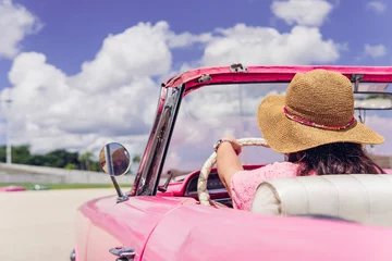 Papier Peint photo Havana Anonymous female traveler in straw hat driving pink retro cabriolet on cloudy day during summer vacation in Cuba. Unrecognizable woman driving retro cabriolet on city road
