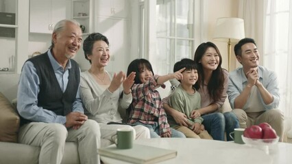 happy three generation asian family sitting on couch in a row watching sport broadcasting on tv at home - Powered by Adobe