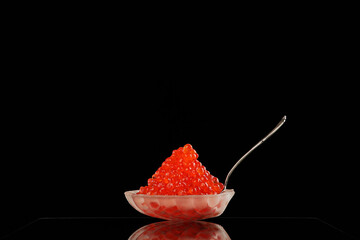 Red caviar.Caviar in a transparent dish in the form of a shell on black background. An exquisite snack. Side view. Space for copying.