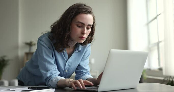 Young serious pensive girl working on laptop, ponders, reflects while makes creative university assignment, typing essay or summary, thinking over solution, looks thoughtful. Workflow using technology