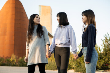 3 girls with Asian features walk down the street holding hands. Urban lifestyle and outdoor activity concept.