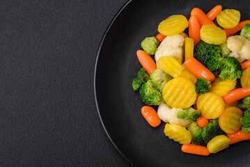 Delicious fresh vegetables steamed carrots, broccoli, cauliflower on a black plate