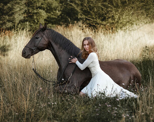 Beautiful girl on the lawn with a horse that lies - 575415027