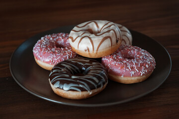 multi-colored, white, pink, chocolate donuts lie on a brown plate. Vegetarian breakfast, sweet. High quality photo