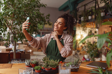 Smiling woman florist taking selfie with her plants for publishing in social media