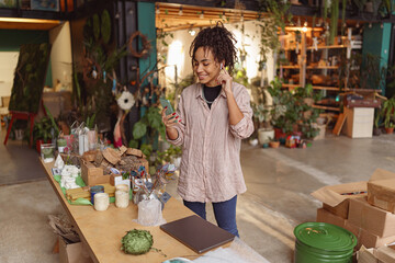 Smiling woman florist decorator listening music during break in floral studio