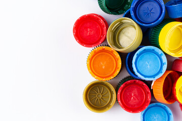 Multicolored plastic bottle caps are scattered on a white background. Plastic recycle place for text.