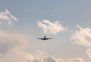 Two aircrafts taking off at Stuttgart Airport, against bright cloudy sky. The silver aircraft ist reflecting the sun
