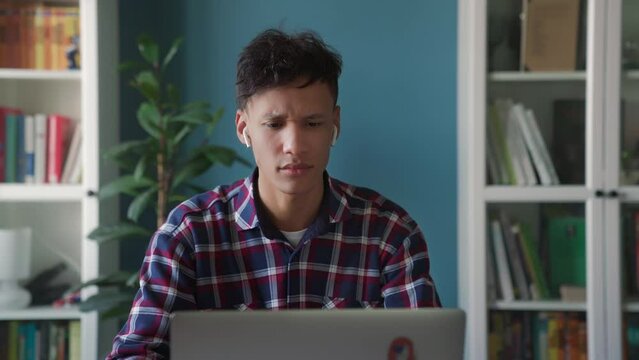 Portrait of focused professional using laptop in stylish apartment. Millennial guy studying online and nervous about failure. Young manager freaking out while working on a laptop at a remote workplace
