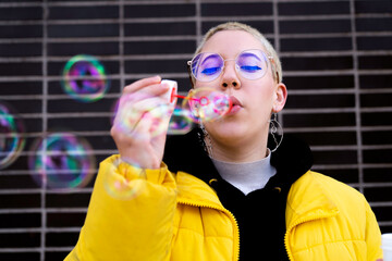 young woman LGBT with curvy blonde short hair blowing soap bubbles