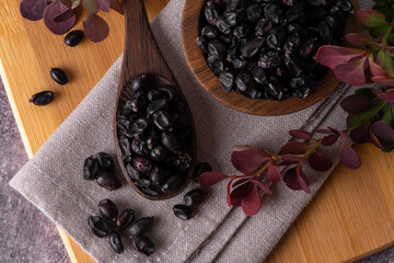 Berries of black barberry in wooden bowl and spoon. Spice barberry blue. Dry berries of barberries.